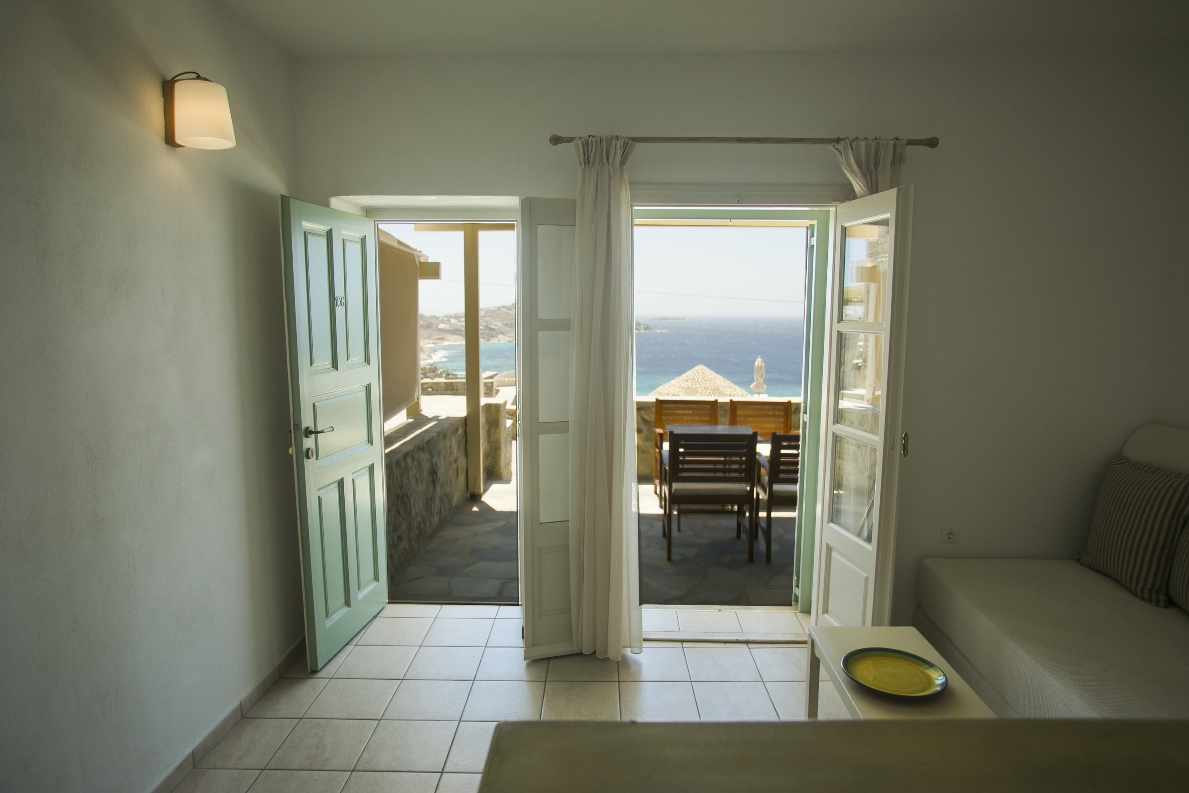 Open green doors leading to outdoor seating and a sea view