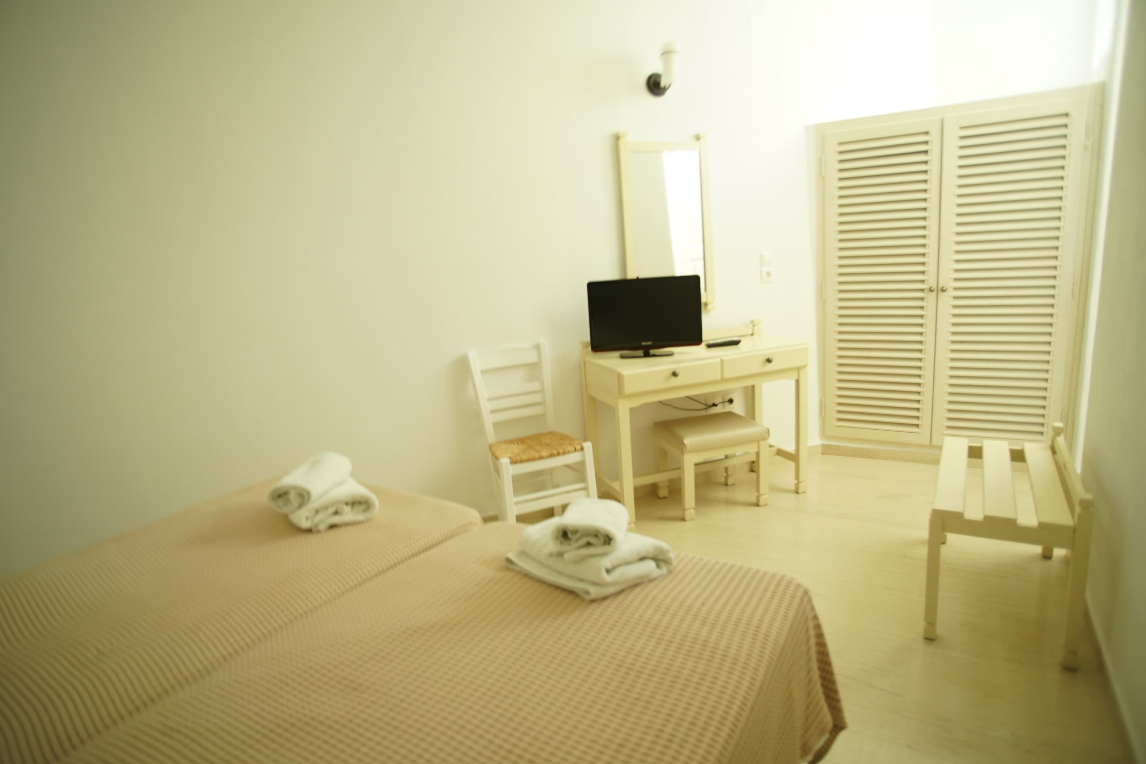 Beds with folded towels facing a television and louvred cupboards